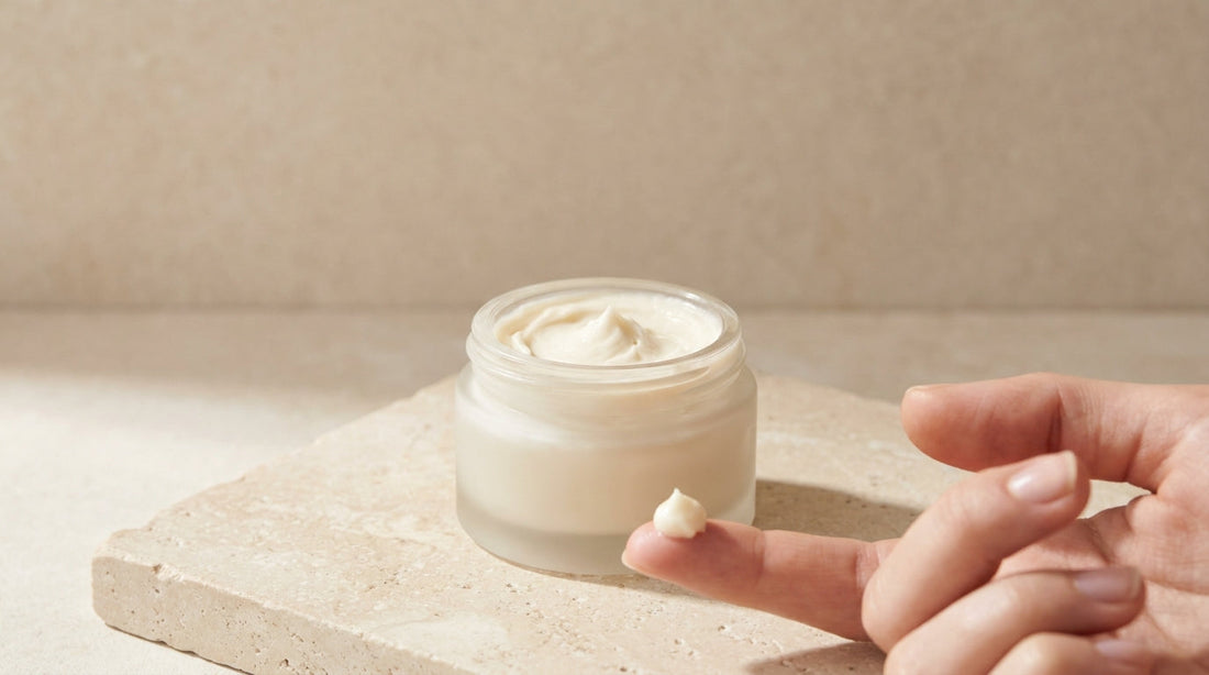 Pea-sized amount of whipped grass-fed tallow balm on a fingertip beside an open jar